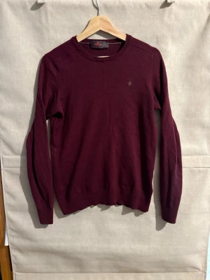 Vinröd stickad tröja från Morris - Snygg vinröd stickad tröja från Morris i 100% merinoull. Tröjan har rund halsringning, diskret logga broderad på bröstet och ribbade muddar vid ärmslut. Perfekt för dig som gillar klassisk och stilren design. Tröjan är i storlek medium men passar small