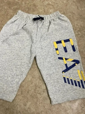 Gråa mjukisbyxor med tryck - Gråa mjukisbyxor med resår i midjan och snörning. Stort grafiskt tryck i blått och gult på ena benet. Tillverkade i mjukt och bekvämt sweatmaterial, perfekta för en avslappnad stil.