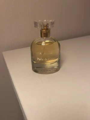 Perle de Coco Eau de Toilette - Perle de Coco Eau de Toilette från & Other Stories. Doften är fruktig med toppnoter av karamell och rött äpple, hjärtnoter av bambu, jasmin och ylang samt basnoter av vanilj, sandelträ och varm mjölk. Flaskan är genomskinlig med guldfärgad detalj och elegant rund form. 