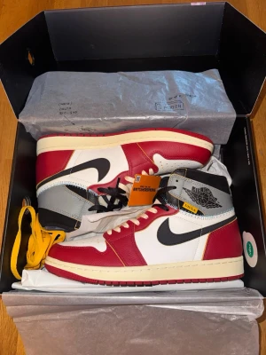 Nike Air Jordan 1 Retro High Union - Grymma Nike Air Jordan 1 Retro High Union sneakers i vitt, rött, svart och grått läder i stl 45. Klassisk high-top siluett med kontrasterande sömmar och detaljer. Kommer med extra gula skosnören och originalkartong. Perfekta för dig som vill sticka ut med din sneakerstil. Köpta på Sneakerhyllan. 