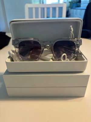 Genomskinliga solglasögon från chimi  - Snygga solglasögon från chimi med genomskinlig, fyrkantig båge och mörka glas. Kommer i original vit hård väska och med tygpåse. Perfekta för att höja din stil på sommaren. Varan är helt ny aldrig använda.