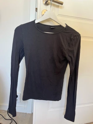 Svart långärmad topp Gina Tricot - En enkel och stilren grå långärmad topp från Gina Tricot. Modellen har rund halsringning och är figurnära i passformen. Perfekt basplagg att matcha med allt. Tillverkad i mjuk bomullsmix för skön känsla.