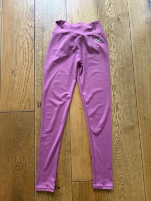 Lila leggings från EVOLVE - Säljer ett par rosa leggings från EVEpeach med hög midja och scrunch-detalj bak. Rosett knyts ovanför scrunch. De är tighta, men stretchiga, perfekta för träning. Aldrig använda, endast provade. Ärliga och snabba affärer uppskattas:)