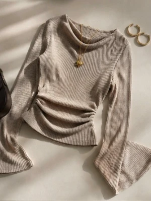  ribbad topp - Trendig beige ribbad topp med långa trumpetärmar och draperad midja. Mjuk och stretchig kvalitet som sitter snyggt på kroppen. Perfekt till jeans eller kjol🩷
