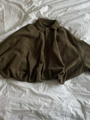 Olivgrön mockajacka med dragkedja - Snygg olivgrön mockajacka med dragkedja och klassisk krage. Jackan har en loose passform och är perfekt för dig som gillar en avslappnad stil. Materialet är mjuk mocka som ger en lyxig känsla.