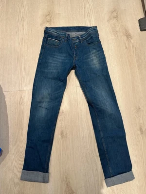 Blå raka jeans med uppvik - Säljer ett par klassiska blå jeans med raka ben i stilen slim. Jeansen har fem fickor och subtila slitningar framtill för en avslappnad look. Perfekta till vardags och passar till det mesta. Materialet är denim i bomull. Sparsamt använda. Märket är Replay. Är 183 cm lång och bär storlek S/M. W32. 