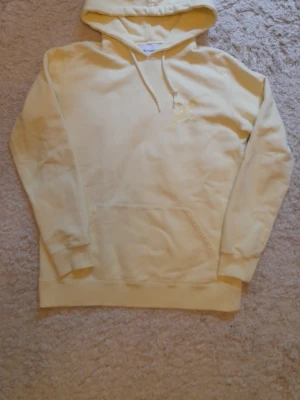 Gul hoodie från Axel Arigato - Ljusgul hoodie med broderad fågel på bröstet från Axel Arigato. Klassisk känguruficka framtill, ribbade muddar och justerbar huva med dragsko. Tillverkad i mjukt bomullsmaterial för en skön och avslappnad look.