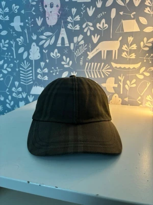 Mörkgrön keps med ton-i-ton mönster - Snygg mörkgrön keps med diskret ton-i-ton rutmönster. Klassisk böjd skärm och justerbar rem bak för perfekt passform. Tillverkad i ett slitstarkt tyg som känns både stilrent och avslappnat.
