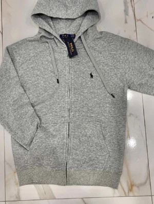 Grå Polo Ralph Lauren kofta - Snygg grå hoodie från Polo Ralph Lauren med dragkedja och huva. Klassisk logga broderad på bröstet, ribbade muddar och snörning i huvan. Tillverkad i mjuk bomullsmix som är perfekt för chill dagar eller när du vill ha en clean look. Koftan säljs pga fel storlek vid köp. Färgen på bilden ser lite mörkare ut, den ska vara lite ljusare 