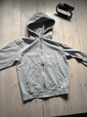 Grå zip hoodie från Weekday - Snygg grå zip hoodie från Weekday med huva och dragsko. Tillverkad i mjukt sweatshirtmaterial och har två stora fickor framtill. Perfekt för en avslappnad och stilren look.