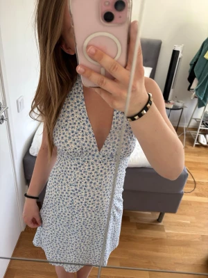 Blå blommig klänning - Blå blommig miniklänning med halterneckmodell och knytning i nacken! Köpt på H&M.