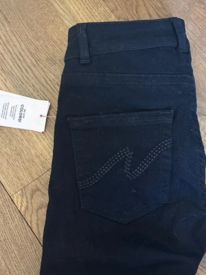 Svarta bootcut jeans från Nelly - Snygga svarta bootcut jeans från Nelly med låg midja och klassisk femficksdesign. Jeansen har en diskret dekorsöm på bakfickan och är perfekta för dig som gillar en tidlös look. Tillverkade i stretchigt material för extra komfort.