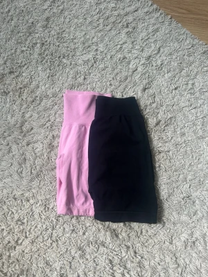 Två par  träningsshorts - Säljer två par träningsshorts, ett par i ljusrosa och ett par i svart. tillverkade i stretchigt material som passar perfekt för gymmet eller löpning. Båda är utan synliga loggor och har en tight passform. 75kr för båda.