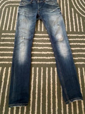 Blå slitna jeans från Dundup - Säljer ett par blå jeans från Dondup med slitningar på benen för en cool, avslappnad look. Jeansen har fem fickor, raka ben och detaljerade sömmar på bakfickan. Materialet är klassisk denim i bomull. W31 L32
