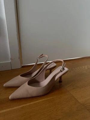 Beige slingback pumps med smal klack - Snygga beige pumps med spetsig tå och smal klack. Skorna har öppen häl med justerbar rem och spänne. Tillverkade i ett slätt material som ger en stilren look. Perfekta för dig som gillar klassisk och trendig stil. Använda en gång