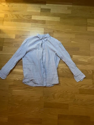 Blårandig linneskjorta från H&M Slim Fit - Säljer en blårandig skjorta från H&M i modellen Slim Fit. Skjortan har långa ärmar, klassisk krage och knäppning framtill. Tillverkad i ett mjukt bomullstyg som känns skönt mot huden. Perfekt för dig som gillar en clean och stilren look.