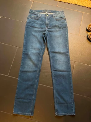 Jeans från MAC Jeans - Säljer ett par klassiska blå jeans från MAC Jeans, modell DREAM. Jeansen har rak passform, fem fickor och stängs med dragkedja och knapp. Perfekta till vardagslooken och tillverkade i ett mjukt denimtyg som sitter skönt hela dagen. Helt nya med alla lappar kvar. Köpta för 1500kr, säljs för 1000kr