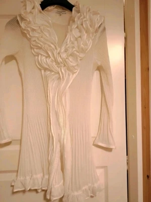 Vintage vit lång kofta med volangkant💎  - Säljer en vit lång kofta med ribbad struktur och stora volangdetaljer längs kragen och framtill😍 Koftan har långa ärmar och volangkant även vid ärmslut och nederkant. Perfekt för dig som gillar romantisk och unik stil🤍😘 XS-M. 
