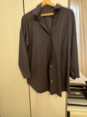 Grått ribbat set med skjorta & byxa - Snyggt tvådelat set i grått med ribbad struktur. Setet består av en långärmad skjorta med knappar och en matchande byxa med resår och dragsko i midjan. Perfekt för en chill och stilren look.