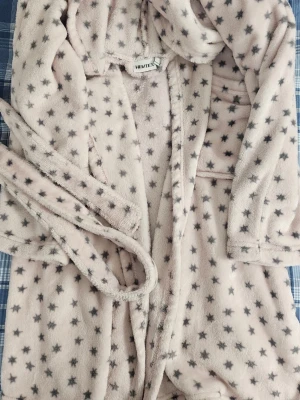 Mjuk morgonrock med stjärnor från Hemtex - Supermjuk beige morgonrock från Hemtex med grå stjärnmönster. Har huva, fickor och knytskärp i midjan. Perfekt för mysiga hemmakvällar och lata morgnar. Tillverkad i fluffigt fleece-material som känns riktigt skönt mot huden.