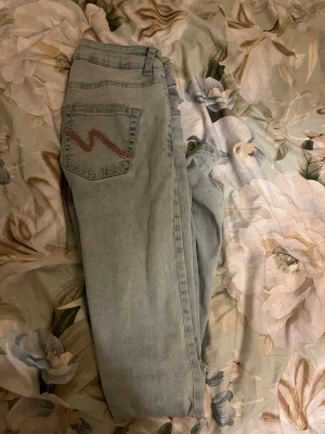 Ljusblå jeans från Nelly.com - Säljer ett par ljusblå jeans från Nelly.com i storlek EU 36. Jeansen har en klassisk femficksmodell med en röd broderad detalj på bakfickan. Perfekta för en avslappnad och trendig look. Materialet är mjukt denim. Dem har slitningar nere vid benen men inget som märks när man använder byxorna