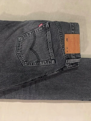 Levi's 501 svarta raka jeans - Säljer ett par klassiska Levi's 501 jeans i svart tvätt med raka ben och femficksmodell. Jeansen har den ikoniska läderpatchen bak i midjan och röd Levi's-tag på bakfickan. Tillverkade i slitstark denim, perfekta för en avslappnad och tidlös stil.