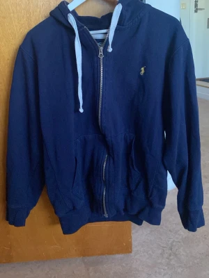 Mörkblå Ralph Lauren hoodie. Storlek L - Mörkblå hoodie med dragkedja och vita snören i huvan. 
