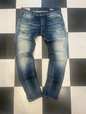 Replay Anbass - Säljer ett par blå slim fit jeans från Replay med snyggt slitna detaljer och klassisk design. Jeansen har ljusa partier på framsidan och bakfickor med broderade sömmar. Materialet är denim i bomull och passformen är slim
