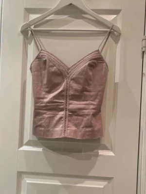 Beige linnetopp med spetsdetaljer - Snygg beige linnetopp med tunna axelband och v-ringning. Toppen har spetsdetaljer längs ringningen och en figurnära passform. Dragkedja baktill för enkel påklädning. Perfekt att styla med jeans eller kjol.