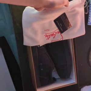 Mörkblå Christian Louboutin sneakers - Exklusiva sneakers från Christian Louboutin i mörkblått med den ikoniska röda sulan. Skorna har snörning och är tillverkade i ett lyxigt material som ger en clean och modern look. Perfekta för dig som vill sticka ut med en klassisk designerstil. (Boxen ser ut så på andra bilden för att kameran fyllde i den med färgen den trodde det var, säg bara till om du vill ha fler bilder. Kommer inte vara lika professionella dock.)