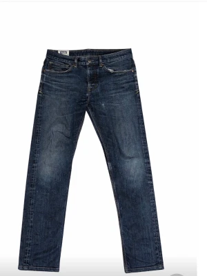 Mörkblå raka jeans från Koi feta slitningar - Snygga mörkblå jeans från Koi med raka ben och klassisk femficksdesign. Jeansen har subtila slitningar och kontrastsömmar, samt en patch med logga bak i midjan. Perfekta för en avslappnad och trendig look. Ett hål i vänster ficka.