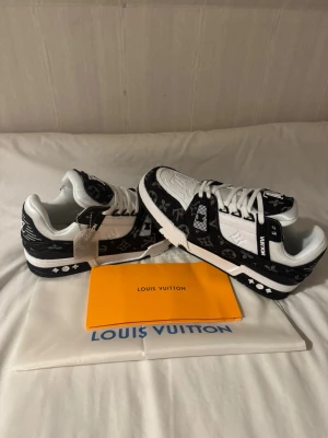 Louis Vuitton svartvita sneakers - Snygga Louis Vuitton sneakers i svart och vitt med klassiskt monogrammönster. Skorna har vita detaljer, svarta sulor med logotyp och är tillverkade i en mix av läder och textil. Tydliga LV-detaljer på sidan och tungan ger en exklusiv känsla. 