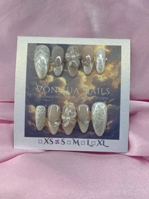 SilkBloom (S);Medium Almond - Unika handgjorda press-on naglar i en medium lång mandelform. Setet har en mix av pärlemor, skimrande guld och nude färg, dekorerade med kristaller och 3D-blommor. Perfekt för dig som vill ha något unikt och glamoröst. S: 15 mm, 11,5 mm, 12 mm, 11 mm, 9 mm 