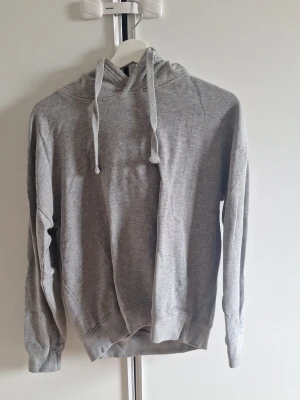 Grå hoodie med huva och dragsnören - En enkel och stilren grå hoodie med huva och dragsnören. Tröjan har långa ärmar, ribbade muddar. Lager 157