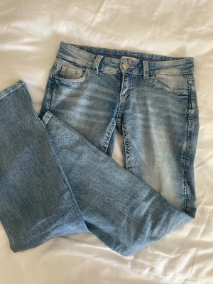 Low waist ljusblå jeans med detaljer  -  Low wasted, bootcut jeans med hål och detaljer på fickorna. Säljer då det är för korta men inga andra deffekter. Midjemått tvärsöver: 37 cm, innerbenenslängd: 78 cm. Tryck gärna på köp nu! 