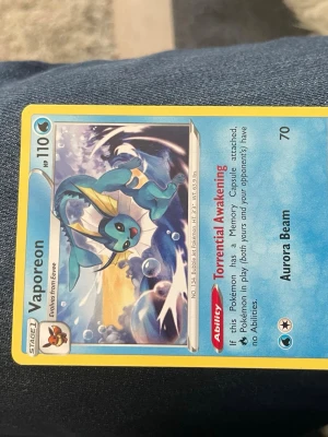 Vaporeon Pokémonkort - Säljer ett Vaporeon Pokémonkort med blå och gula detaljer. Kortet har 110 HP och visar Vaporeon i vattenmiljö. Det har förmågan Torrential Awakening och attacken Aurora Beam. Perfekt för samlare eller Pokémonfans.