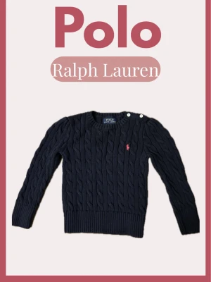 Barn Mörkblå kabelstickad tröja Polo Ralph Lauren - Mörkblå kabelstickad tröja från Polo Ralph Lauren med rund halsringning och två vita knappar på axeln. Tröjan har det klassiska rosa Polo-logot broderat på bröstet och ribbade muddar vid ärmslut och nederkant. Perfekt för dig som gillar tidlös och stilren design.