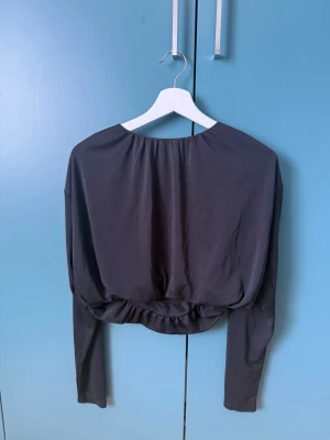 Croppad topp - Säljer en svart croppad topp med långa ärmar och rund halsringning. Toppen har en loose passform och är tillverkad i ett mjukt, stretchigt material som känns skönt mot huden. Perfekt att styla med höga jeans eller kjol.