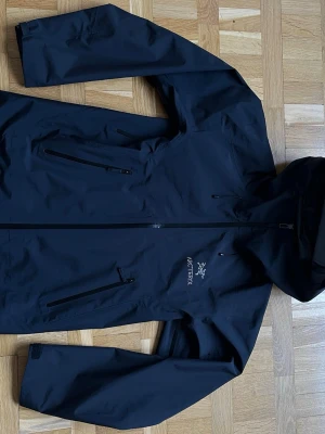 Arc’teryx Beta LT Gore-Tex Jacka M - Snygg svart regnjacka från Arc'teryx med huva och dragkedja framtill. Jackan har flera praktiska fickor med dragkedja och är tillverkad i ett vattentätt material. Perfekt för regniga dagar och outdoor-äventyr.