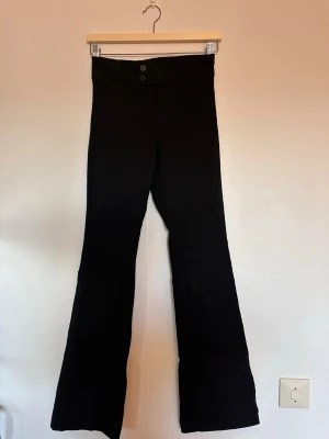 Svarta bootcut byxor med hög midja - Virala bershka kostymbyxorna. Snygga svarta byxor med bootcut-modell och mid  waist. Byxorna har två knappar framtill och en ficka med lock bak. Perfekta för dig som gillar en klassisk men trendig look.