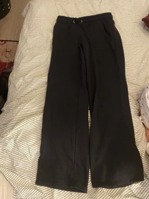 Svarta vida mjukisbyxor - Säljer ett par svarta mjukisbyxor med breda ben och dragsko i midjan. Byxorna har två stora fickor framtill och är gjorda i ett mjukt och bekvämt material, perfekt för chill dagar. Passar dig som gillar en avslappnad och trendig look.