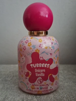 Tubbees Unicorn Vanilla parfym - Söt parfymflaska från Tubbees med doften Unicorn Vanilla. Flaskan är rosa med färgglada blommor, regnbågar och enhörningsmotiv samt en stor rund rosa kork. Perfekt för dig som gillar lekfulla och söta dofter.