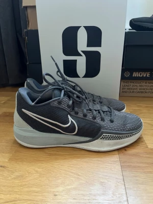 Sabrina 1 Beyond The Game sneakers - Säljer ett par snygga Nike sneakers i grått och svart med vit swoosh på sidan. Skorna har låg profil, mesh- och syntetmaterial på ovandelen samt cool textur på tån. Perfekta för dig som gillar stilrena och sportiga skor. PRIS KAN DISKUTERAS 