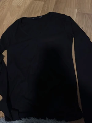 Svart långärmad topp från 157 - En enkel och stilren svart långärmad topp från 157. Toppen har v-ringning och är tillverkad i ett mjukt material som känns skönt mot huden. Perfekt att matcha med jeans eller kjol för en clean look.