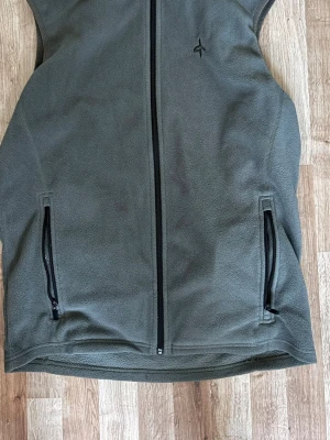 Olivgrön fleeceväst Cross Sportswear - Olivgrön fleeceväst från Cross Sportswear med hel dragkedja framtill och två fickor med dragkedja. Västen har ett diskret logotryck på bröstet och är tillverkad i mjukt fleecematerial. Perfekt för lager-på-lager och outdoor.