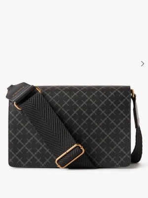 Svart axelväska från By Malene Birger - Snygg svart axelväska från By Malene Birger med grafiskt mönster i grått. Väskan har bred justerbar axelrem i textil och guldfärgade metalldetaljer. Tillverkad i konstläder med två fack invändigt och magnetlås. Perfekt för dig som gillar stilrena accessoarer.