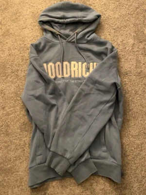 Blå HOODRICH hoodie - Snygg blå hoodie från hoodrich med broderad logga i vitt framtill. Klassisk modell med huva och dragsnören, samt ribbade muddar vid ärmslut och nederkant. Perfekt för en avslappnad streetwear-look. Snörena är slitna 