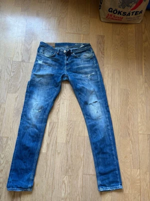 Blå slitna jeans från Dondup - Snygga blå jeans med slitningar och lätt tvättad look. Jeansen har smal passform, klassiska fem fickor och dragkedja med knapp. Perfekta för en avslappnad och trendig stil.