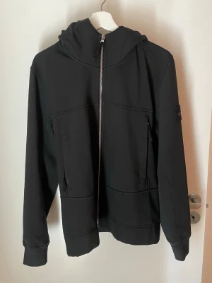 vindjacka - Stone Island - Snygg marinblå/mörkblå herr vindjacka från Stone Island med huva och dragkedja framtill. Jackan har klassisk patch på ärmen och sportiga ränder på huvkanten. Den har inga defekter eller slitage enbart lite urtvättad. 