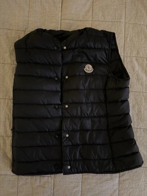 Svart monclerväst - Svart tunn Moncler väst i dun, använd endast ett fåtal gånger och i mycket fint skick. Storlek 2, passar ungefär S-M. Perfekt som lager-på-lager eller som lätt ytterplagg. Säljes då den tyvärr inte kommer till användning. Kan mötas på Östermalm. Nypris 7500